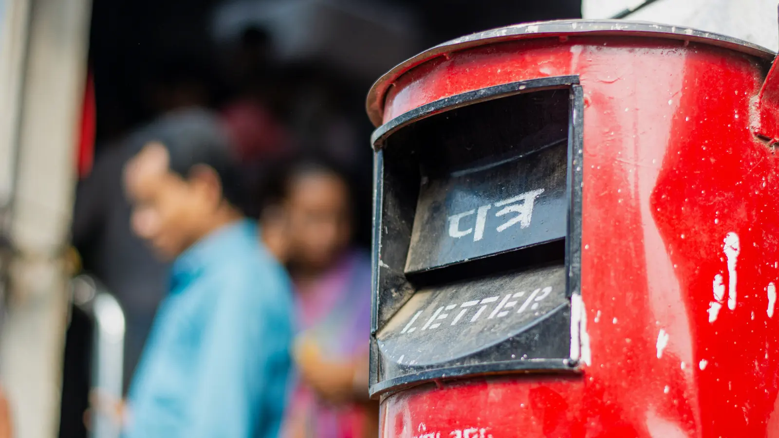 Red India Post letter box with people blurred behind