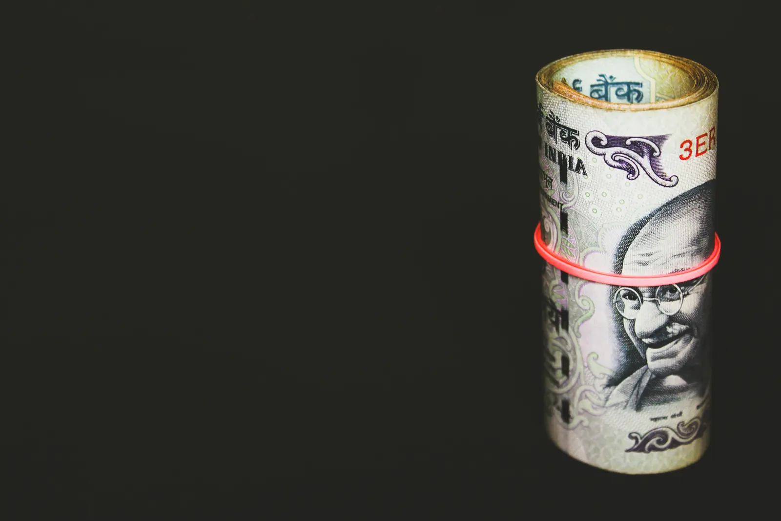 Single rolled rupee note showing Gandhi on black