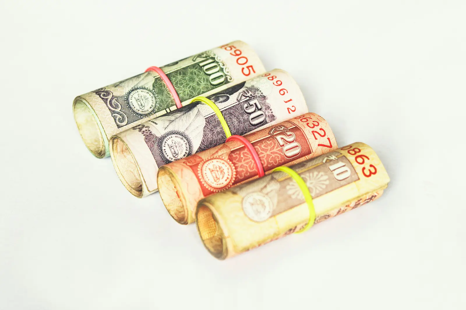 Four rolled rupee notes laid diagonally on white
