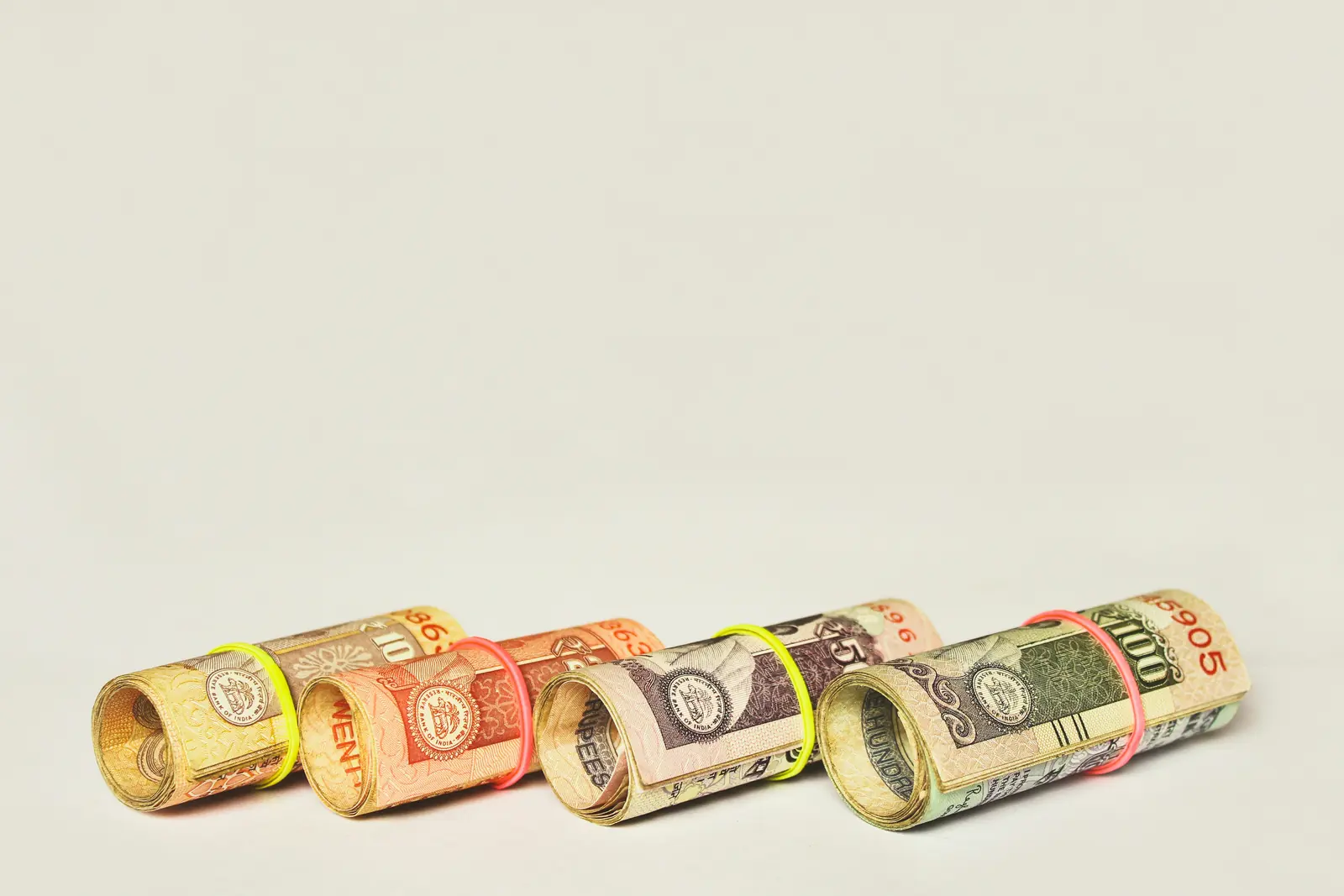 Row of four rolled rupee notes on a white background