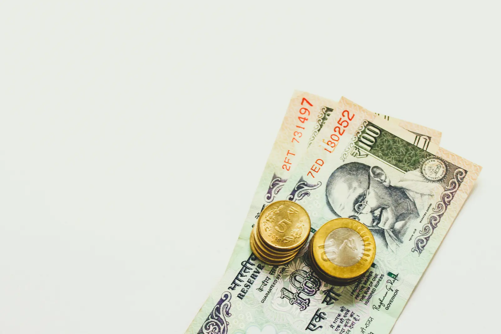 ₹100 notes with rupee coins in the corner of a white frame